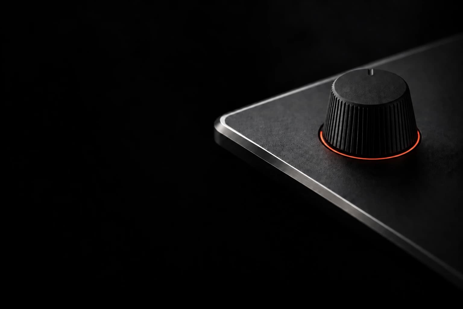 A tapered matte rubber knob with a rear-facing position notch and a continuous thin red LED ring, on a shallow tabletop synthesizer with a silver bevel fading into darkness.